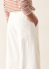 Woman wearing white denim barrel leg trousers with a burnt orange stripe knit sweater and brown belt.