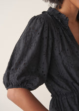 Woman wearing a black maxi broderie dress with deep v-neck against a beige background