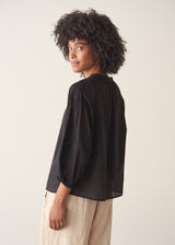 A woman wearing a sheer black embroidered blouse with light linen trousers.