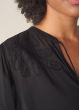 A woman wearing a sheer black embroidered blouse with light linen trousers.