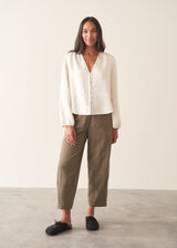 A woman wearing a white long sleeve button-up blouse with a V-neck, paired with khaki green trousers.