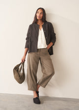 A woman wearing a white long sleeve button-up blouse with a V-neck, paired with khaki green trousers.