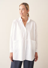 A woman wearing a large white smock shirt with navy blue trousers