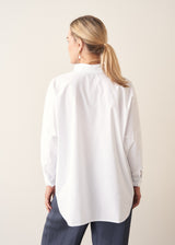 A woman wearing a large white smock shirt with navy blue trousers