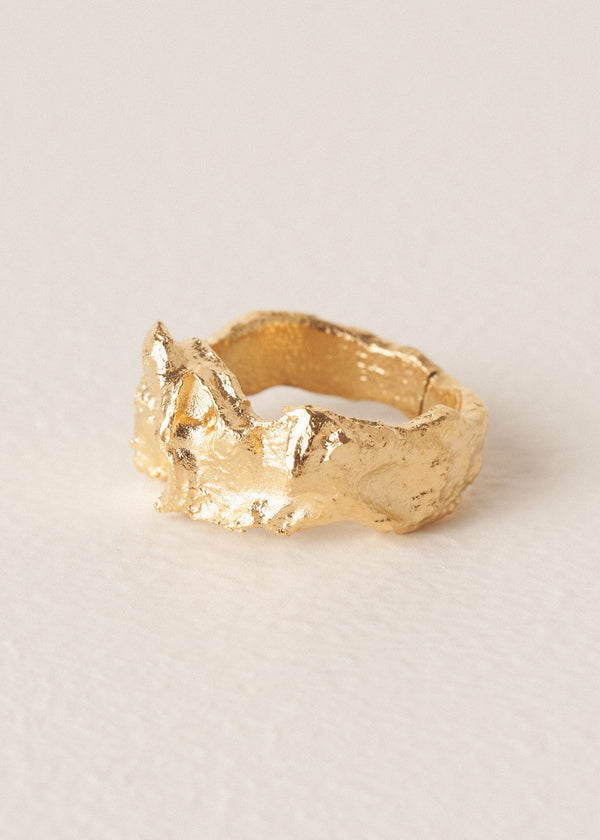 Large, textured molten gold ring on a beige background