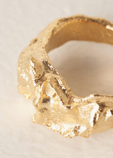 Close-up of large, textured molten gold ring on beige background