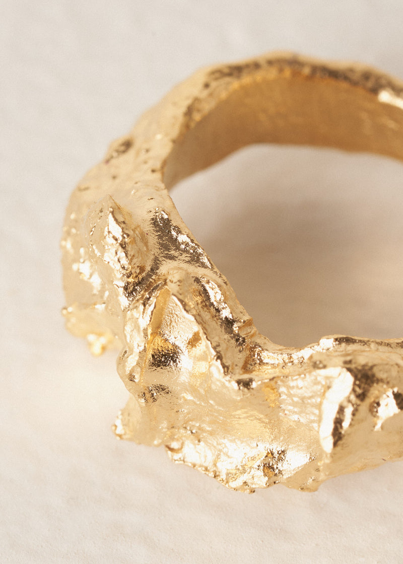 Close-up of large, textured molten gold ring on beige background