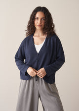 Woman wearing a navy lightweight cardigan with a white tank top and grey striped trousers against a beige background