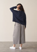 Woman wearing a navy lightweight cardigan and grey striped trousers with white trainers, against a beige background