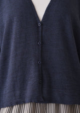 Close up of woman wearing a navy lightweight cardigan with a white tank top and grey striped trousers