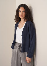 Woman wearing a navy lightweight cardigan with a white tank top and grey striped trousers against a beige background