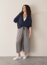 Woman wearing a navy lightweight cardigan with a white tank top and grey striped trousers, paired with white trainers, against a beige background