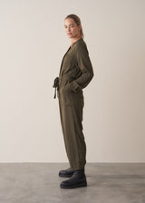 Woman wearing dark khaki relaxed fit jumpsuit with pocket and waist tie