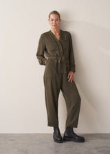 Woman wearing dark khaki relaxed fit jumpsuit with pocket and waist tie