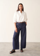 Woman wearing dark blue barrel leg denim jeans with a white cotton shirt.