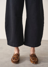 Woman wearing a pair of cropped, black barrel-leg denim jeans with leopard print loafers, against a beige background