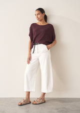 Woman wearing white cropped barrel leg jeans with plum short sleeve top