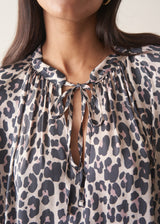 Woman wearing a leopard print blouse and black trousers against a plain background