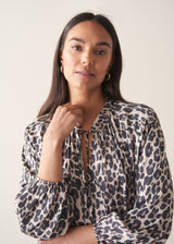 Woman wearing a leopard print blouse and black trousers against a plain background
