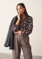 A woman wearing a dark brown deer print  blouse with checked trousers and a dark grey blazer