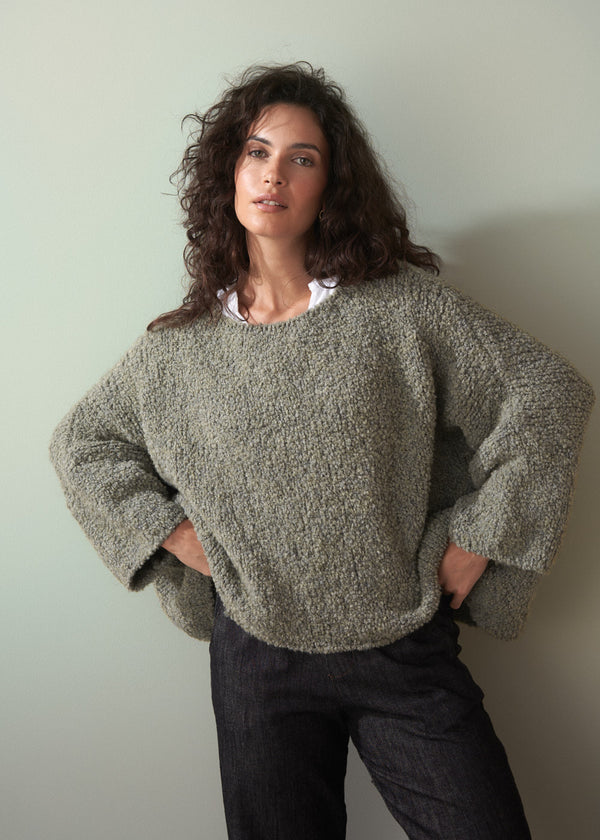 Woman wearing a boucle light green sweater against a plain background