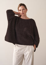 Woman wearing a dark brown boucle sweater and cream trousers against a plain background