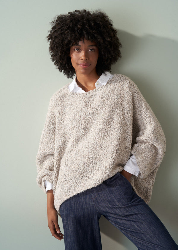 Person wearing an off white boucle sweater and dark blue jeans against a plain background