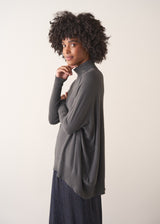 Woman wearing a dark grey turtleneck sweater and blue satin trousers against a plain background