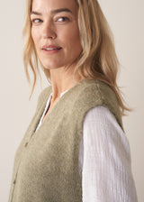 Woman wearing khaki green sleeveless knit waistcoat with blue jeans