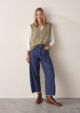 Woman wearing khaki green sleeveless knit waistcoat with blue jeans