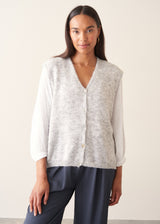 A woman modelling a light grey marled knit waistcoat over a white long-sleeve blouse and navy blue trousers.