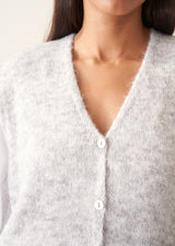 A woman modelling a light grey marled knit waistcoat over a white long-sleeve blouse and navy blue trousers.