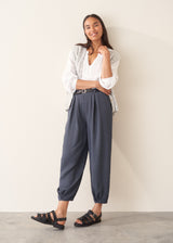 A woman modelling a light grey marled knit waistcoat over a white long-sleeve blouse and navy blue trousers.