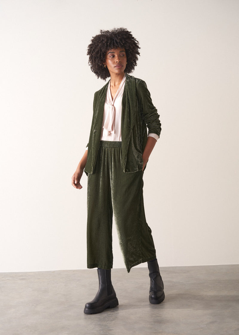 Woman wearing a green velvet blazer and green wide velvet trousers against a white background