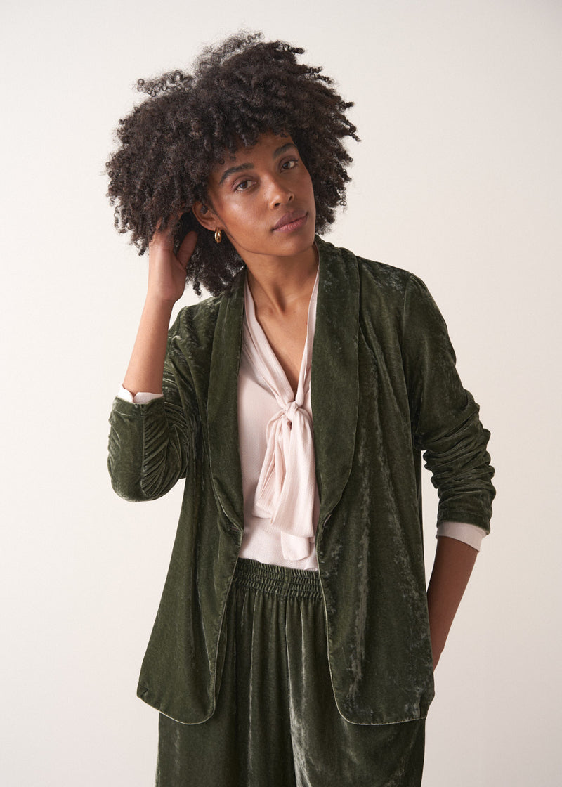 Woman wearing a green velvet blazer and green wide velvet trousers against a white background