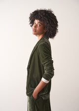 Woman wearing a green velvet blazer and green wide velvet trousers against a white background