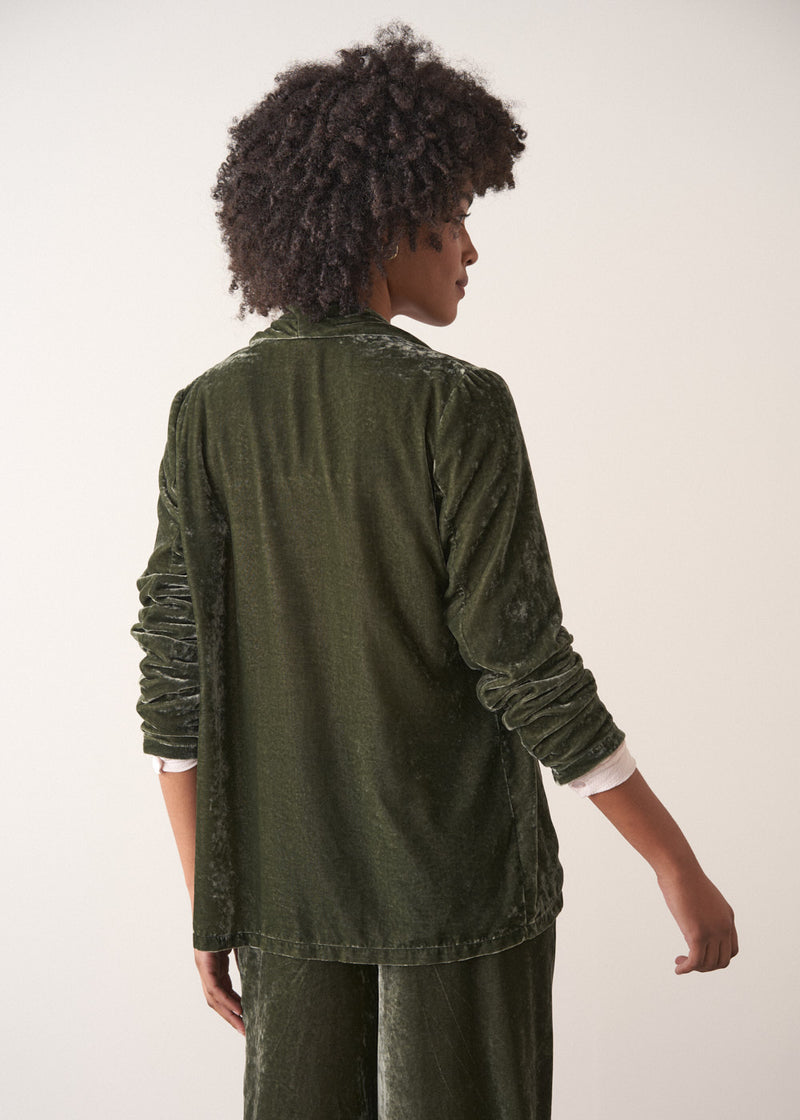 Woman wearing a green velvet blazer and green wide velvet trousers against a white background