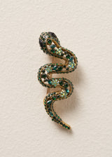 Sparkling snake brooch with twinkling green crystals on a classic pin fastening, photographed on a beige background