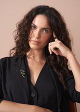 Model wearing a sparkling snake brooch with twinkling green crystals on a classic pin fastening, with a contrasting black blazer