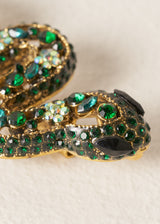 Close up detail of a sparkling snake brooch with twinkling green crystals on a classic pin fastening, photographed on a beige background