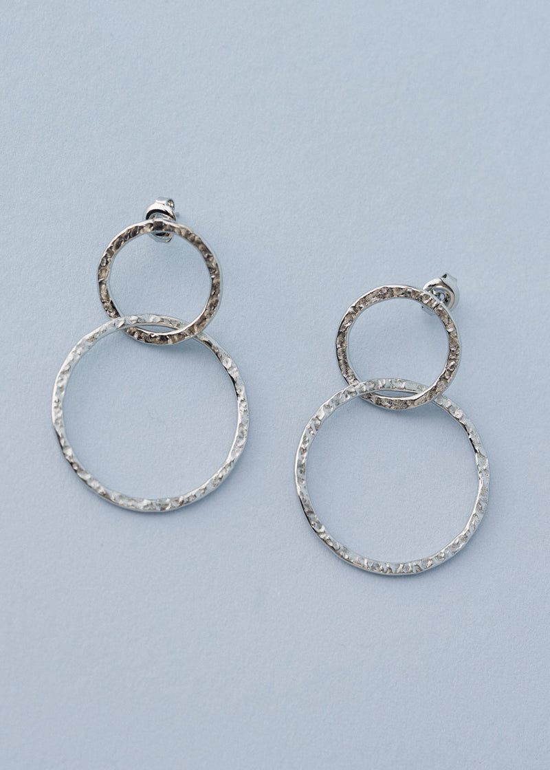 Hammered silver drop earrings with interlocking double hoops on blue background