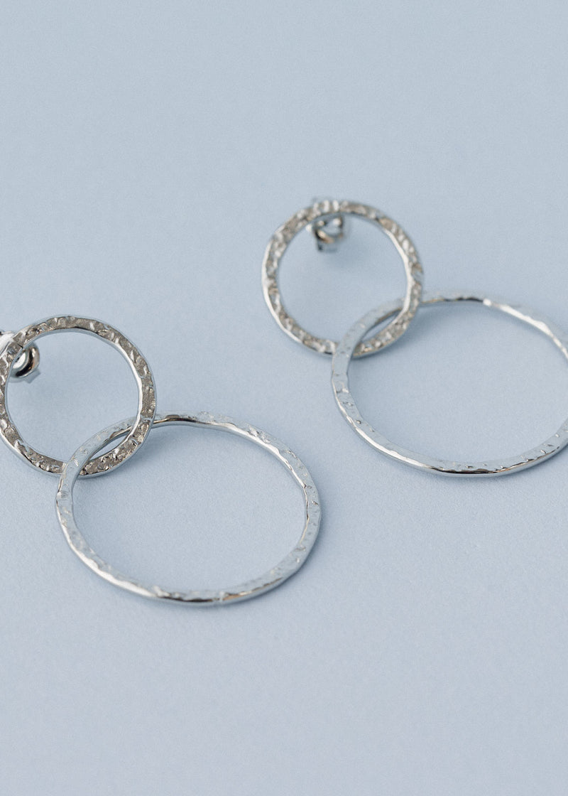 Hammered silver interlocking hoop earrings on blue background
