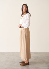 Woman wearing light beige cropped wide leg trousers, matching beige jacket and a white top.
