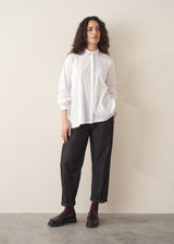 Woman wearing an oversized white shirt and dark jeans, paired with brown loafers and socks