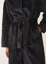 Close up of an oversized black faux fur coat, buttoned with woman's hand in pocket