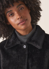 Close up of texture and button detail of a women's black faux fur coat