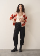 Woman wearing a red and blush pink striped cardigan over white satin top and black drawstring trousers with chunky boots