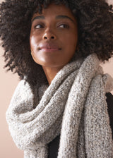 Woman wearing a textured chunky knit scarf in neutral tone, against a neutral background