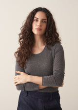 Woman wearing a grey metallic long-sleeve top and dark jeans against a beige background
