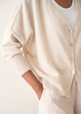 A woman wearing a light oatmeal cream knit cardigan over a white V-neck top and matching light oatmeal trousers.